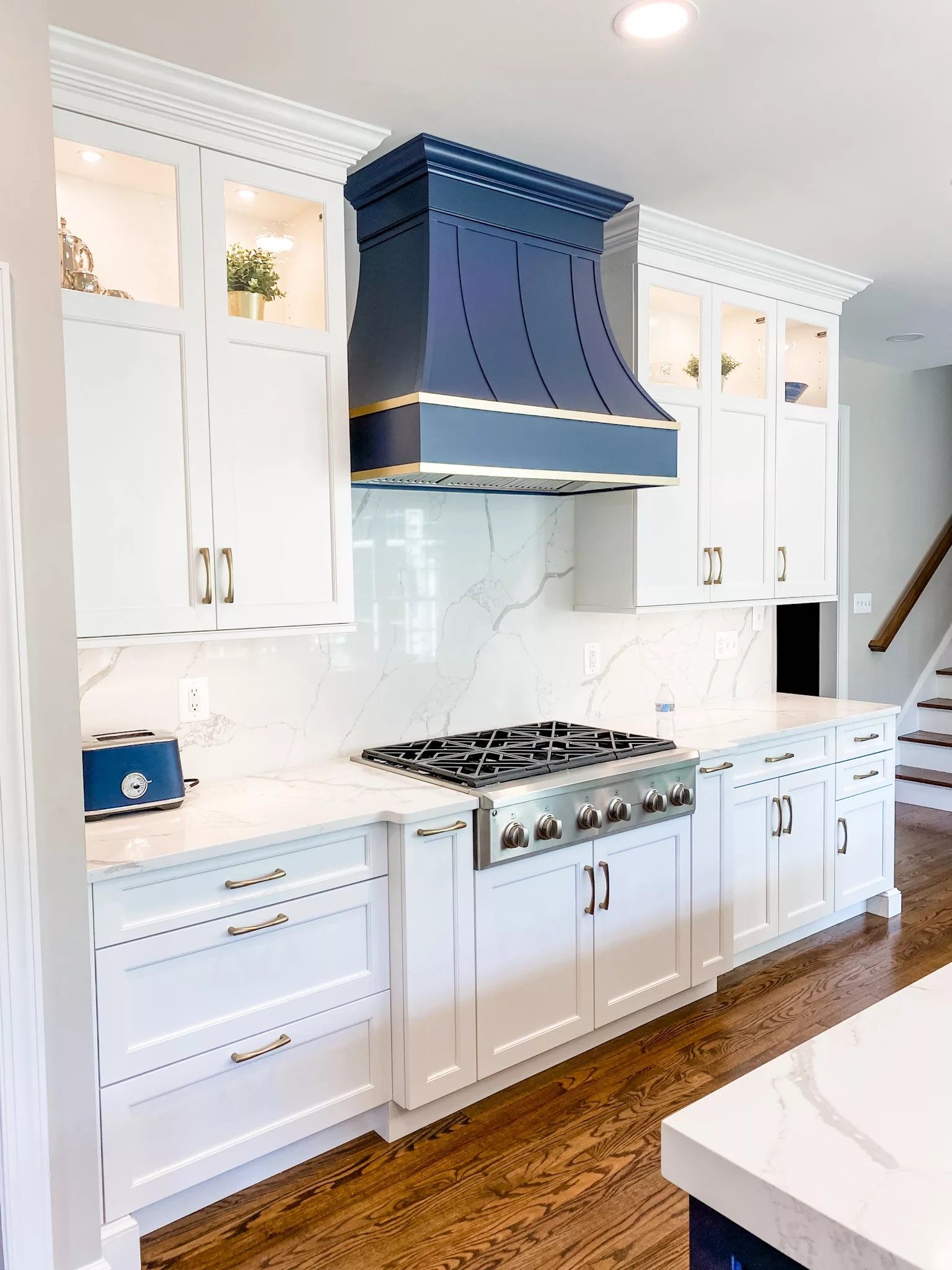 White kitchen with custom navy range hood and marble backsplash